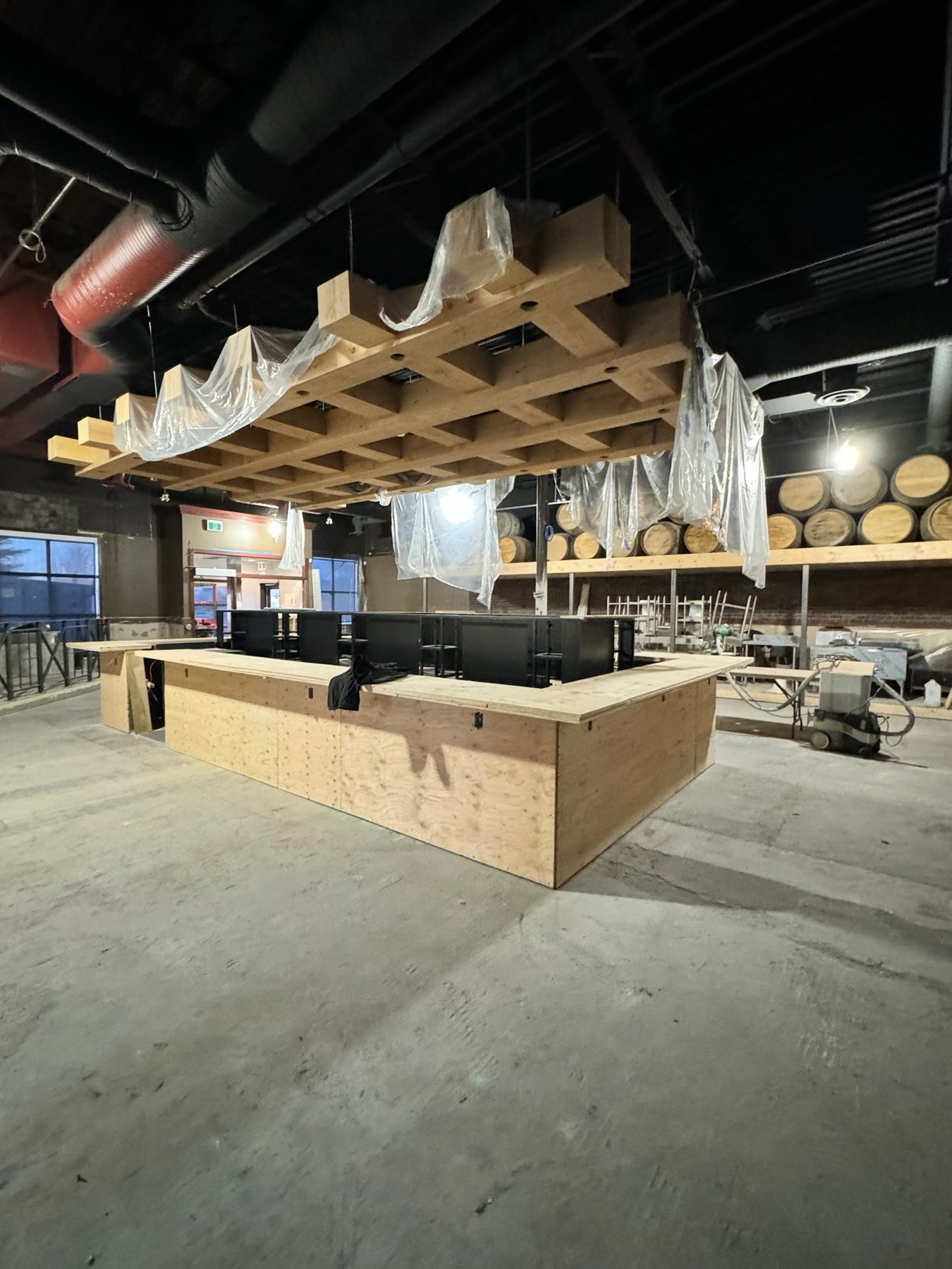 Bar construction with unfinished wood counter, ceiling grid, and barrels — Blowers and Grafton (Medicine Hat) by Onsite Contracting Services